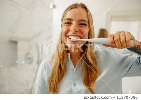 A cheerful woman is happily brushing her teeth in a bright, modernstyle bathroom today 118707386