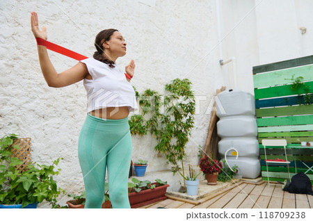Woman exercising with resistance band in outdoor urban garden, promoting fitness and wellness surrounded by plants 118709238