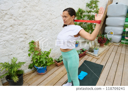 Woman exercising with resistance band in garden for strength and flexibility, showcasing outdoor home workout for fitness and wellness enthusiasts. Woman exercising with resistance band in garden for strength and flexibility, showcasing outdoor home workout for fitness and wellness enthusiasts. 118709241