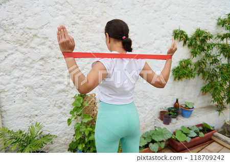 Woman exercising with resistance band in outdoor garden setting for fitness and wellness 118709242