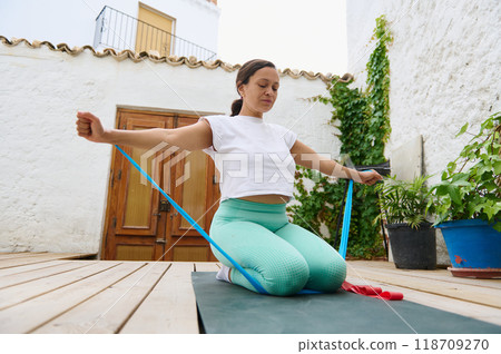 Woman practicing outdoor yoga with resistance band in serene backyard environment 118709270
