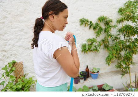 Woman exercising with resistance band in a peaceful garden setting surrounded by plants and greenery Woman exercising with resistance band in a peaceful garden setting surrounded by plants and greenery 118709273