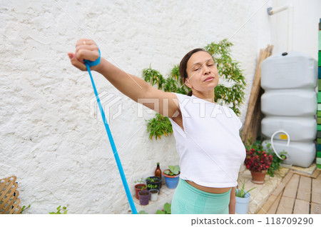 Woman exercising outdoors with resistance band in peaceful garden setting promoting a healthy lifestyle and fitness routine 118709290