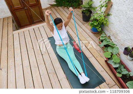 Woman practicing resistance band exercises on an outdoor wooden deck for fitness and wellness Woman practicing resistance band exercises on an outdoor wooden deck for fitness and wellness 118709306