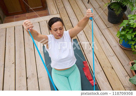 Woman exercising with resistance band on wooden deck, focusing on strength and fitness outdoors 118709308