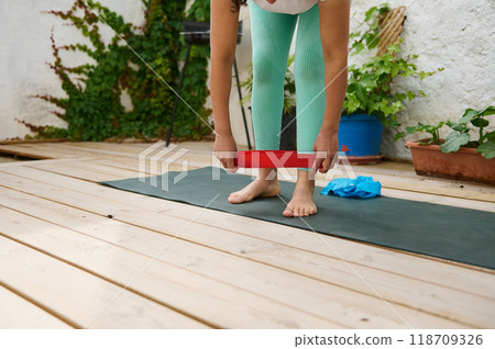 Woman exercising on a wooden deck with resistance band enhancing fitness and flexibility outdoors in a serene garden setting Woman exercising on a wooden deck with resistance band enhancing fitness and flexibility outdoors in a serene garden setting 118709326