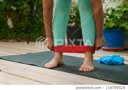 Woman using resistance band during outdoor exercise on yoga mat in garden setting Woman using resistance band during outdoor exercise on yoga mat in garden setting 118709328