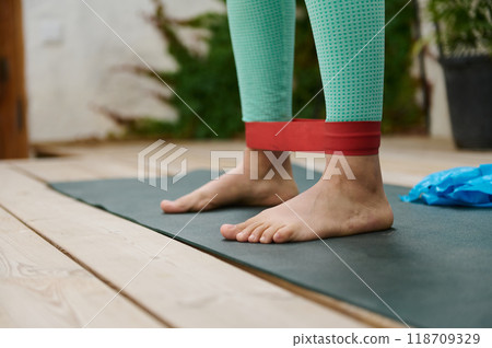 Close-up of person exercising on a yoga mat with a red resistance band outdoors, focusing on fitness and wellness. Close-up of person exercising on a yoga mat with a red resistance band outdoors, focusing on fitness and wellness. 118709329