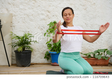 Woman practicing yoga with resistance band in a peaceful outdoor setting for relaxation and fitness Woman practicing yoga with resistance band in a peaceful outdoor setting for relaxation and fitness 118709643