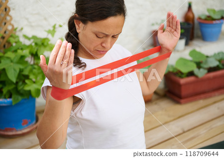 Woman exercising with resistance band in a garden setting, focusing on upper body strength and home fitness. 118709644