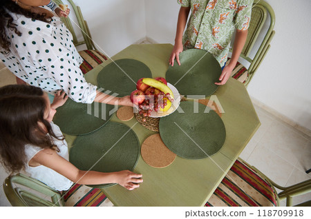 Family preparing a dining table with green mats and fruit centerpiece for a meal gathering at home Family preparing a dining table with green mats and fruit centerpiece for a meal gathering at home 118709918