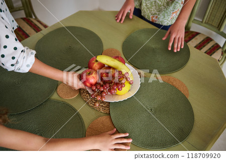 Family preparing dining table with fresh fruit centerpiece for meal gathering, featuring apples, grapes, and banana 118709920