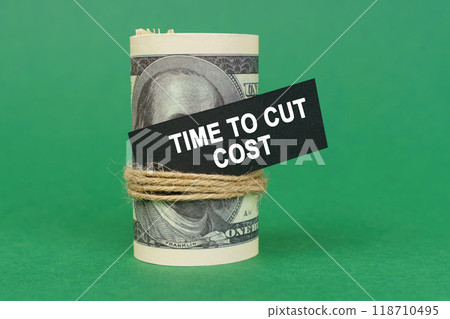 On a green surface, rolled dollars with a black sign that says - Time to cut cost 118710495
