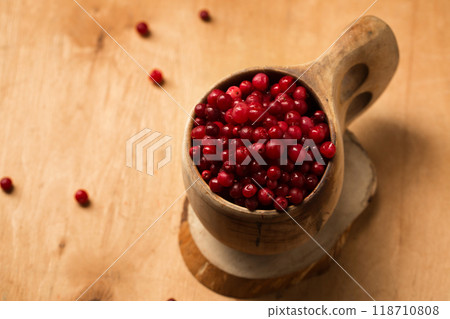 A wooden finnish kuksa full of forest ripe lingonberries on a wooden background A wooden finnish kuksa full of forest ripe lingonberries on a wooden background 118710808