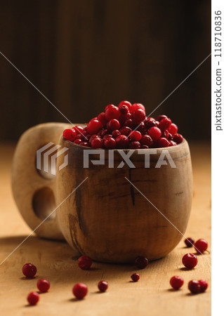 A wooden finnish kuksa cup full of forest ripe lingonberries on a wooden background, close-up A wooden finnish kuksa cup full of forest ripe lingonberries on a wooden background, close-up 118710836