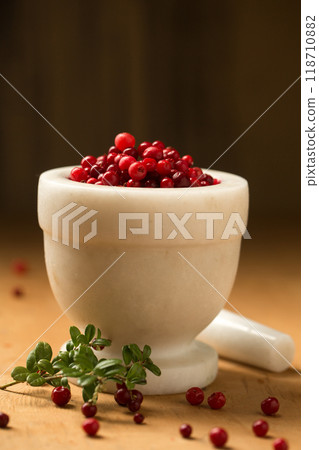A white stone mortar full of wild lingonberries, on a wooden background, low angle A white stone mortar full of wild lingonberries, on a wooden background, low angle 118710882