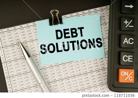 On financial reports lies a calculator, a pen and a sticker with the inscription - Debt solutions On financial reports lies a calculator, a pen and a sticker with the inscription - Debt solutions 118711036