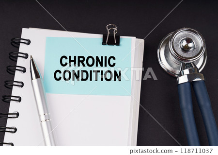 On a black surface, a stethoscope, a notebook, a pen and a blue sticker with the inscription - CHRONIC CONDITION 118711037