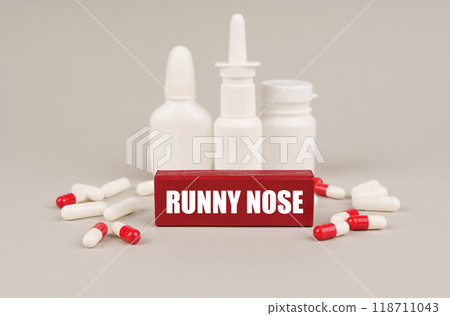 On a gray surface are pills, white jars and a red wooden block with the inscription - Runny nose 118711043
