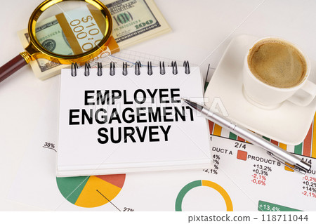 On the table is a cup of coffee, money, business charts and a notepad with the inscription - EMPLOYEE ENGAGEMENT SURVEY On the table is a cup of coffee, money, business charts and a notepad with the inscription - EMPLOYEE ENGAGEMENT SURVEY 118711044