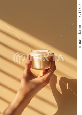 Close-up in the hands of a girl lies a jar of moisturizer on a beige background. The bottle without a label is a mock-up of anti-aging masks, exfoliating cosmetics. The concept of skin care 118711542
