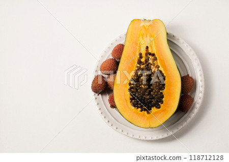 Half of a beautiful juicy ripe papaya and lychee on a white plate on a white table 118712128