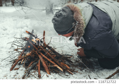 A man makes a fire in the snow in the forest during a winter trip. The man knocks out sparks with a sharp flint trying to make a fire and warm himself. Winter tourism. A man makes a fire in the snow in the forest during a winter trip. The man knocks out sparks with a sharp flint trying to make a fire and warm himself. Winter tourism. 118712722