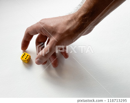 Hand reaching for yellow dice on white background symbolizing chance and decision-making 118713295
