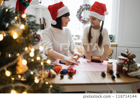 Mother and daughter baking Christmas cookies together in kitchen 118714144