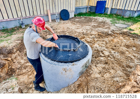 Worker places support ring for manhole cover on concrete septic tank ring. Worker places support ring for manhole cover on concrete septic tank ring. 118715528