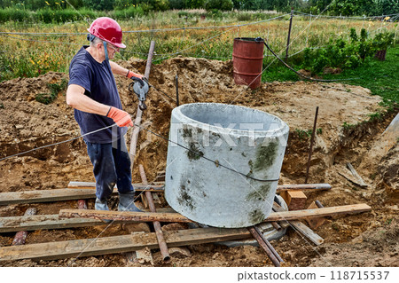 Rigger pushed one concrete ring onto another during construction of septic tank using rollers and winch. Rigger pushed one concrete ring onto another during construction of septic tank using rollers and winch. 118715537