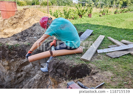 When installing septic tank, builder cuts off piece of plastic sewer pipe with an abrasive saw. 118715539
