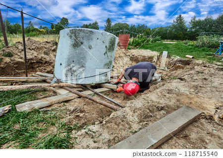 Rigger uses roller bed system and winch to move concrete ring during installation of septic tank. 118715540