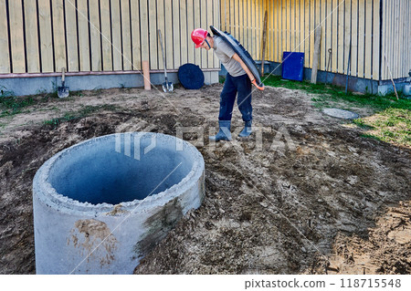 Worker carries heavy support ring for manhole cover to concrete rings of septic tank. Worker carries heavy support ring for manhole cover to concrete rings of septic tank. 118715548