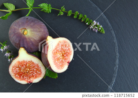 Purple figs on a black stone plate. Photo, background with fresh, juicy, ripe tropical fruits. Suitable for depicting vegetarian and raw, healthy food, harvest. Symbol of abundance and enlightenment. Purple figs on a black stone plate. Photo, background with fresh, juicy, ripe tropical fruits. Suitable for depicting vegetarian and raw, healthy food, harvest. Symbol of abundance and enlightenment. 118715652