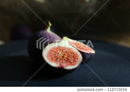 Purple figs on a black stone plate. Photo, background with fresh, juicy, ripe tropical fruits. Suitable for depicting vegetarian and raw, healthy food, harvest. Symbol of abundance and enlightenment. 118715659