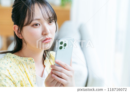 A young woman operating a smartphone in a room 118716072