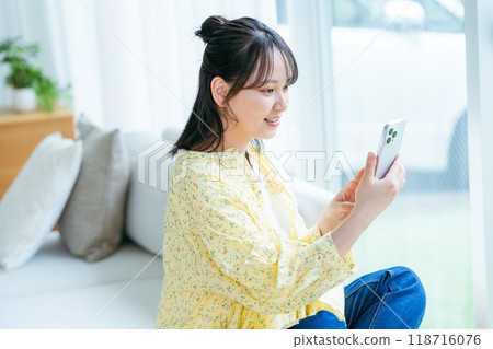 A young woman operating a smartphone in a room A young woman operating a smartphone in a room 118716076