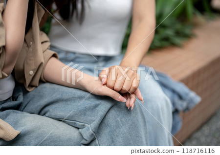 A caring woman holding her sad friend's hand to offer comfort while they converse outdoors. A caring woman holding her sad friend's hand to offer comfort while they converse outdoors. 118716116