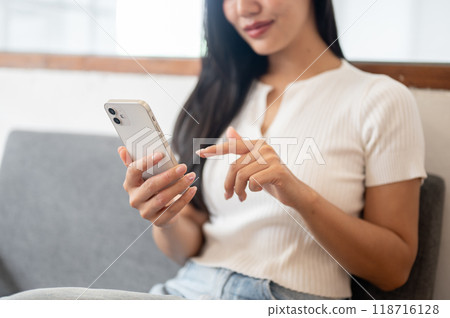 A close-up of a beautiful Asian woman sitting on a sofa in a coffee shop, using her smartphone. A close-up of a beautiful Asian woman sitting on a sofa in a coffee shop, using her smartphone. 118716128