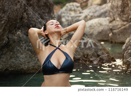 Beautiful girl in a black swimsuit in a blue lagoon among the rocks 118716149