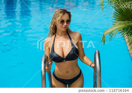 outdoor fashion photo of a beautiful woman with blonde hair wearing a luxurious black swimsuit posing in a swimming pool. Luxurious woman with a beautiful sexy body 118716164