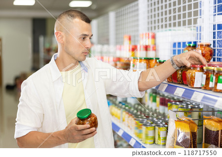 Young man choosing canned pickled vegetables in Asian store Young man choosing canned pickled vegetables in Asian store 118717550