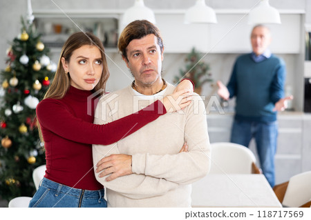 Sad couple listens to their elderly father scream and swear while celebrating Christmas. Family quarrel Sad couple listens to their elderly father scream and swear while celebrating Christmas. Family quarrel 118717569