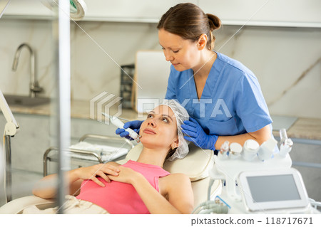Adult woman cosmetologist doing microcurrent procedure to young woman 118717671