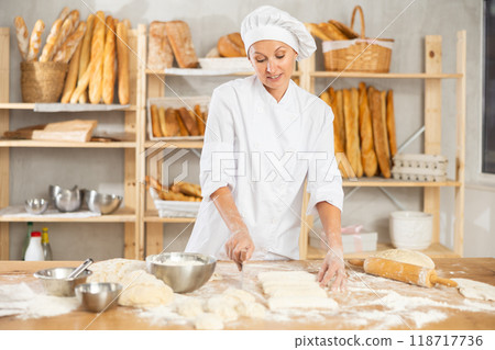 Female employee cooks croissants, rolls dough into tube, forms muffin from raw dough material Female employee cooks croissants, rolls dough into tube, forms muffin from raw dough material 118717736
