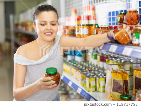 Smiling young Asian woman choosing canned vegetables in supermarket Smiling young Asian woman choosing canned vegetables in supermarket 118717755