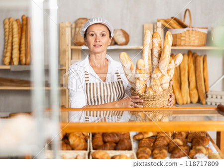 Female baker worker sells baguette, shows many products 118717809