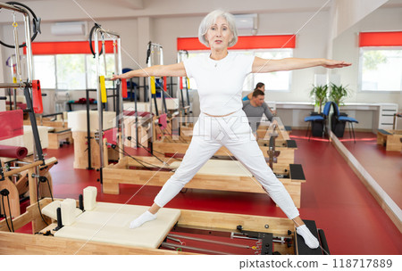 Senior woman performs exercise on reformer to improve coordination, balance, and posture Senior woman performs exercise on reformer to improve coordination, balance, and posture 118717889