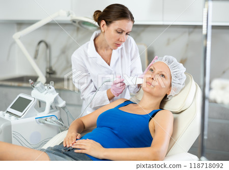 Young beautician doing procedure for face lifting and Soften skin keratin, deep clear skin dirt of adult woman laying in salon. Hardware cosmetology Young beautician doing procedure for face lifting and Soften skin keratin, deep clear skin dirt of adult woman laying in salon. Hardware cosmetology 118718092